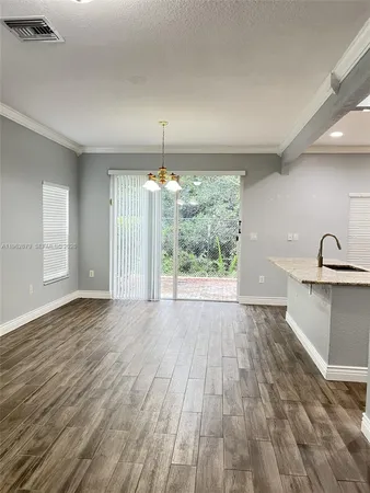 a view of empty room with wooden floor and kitchen view