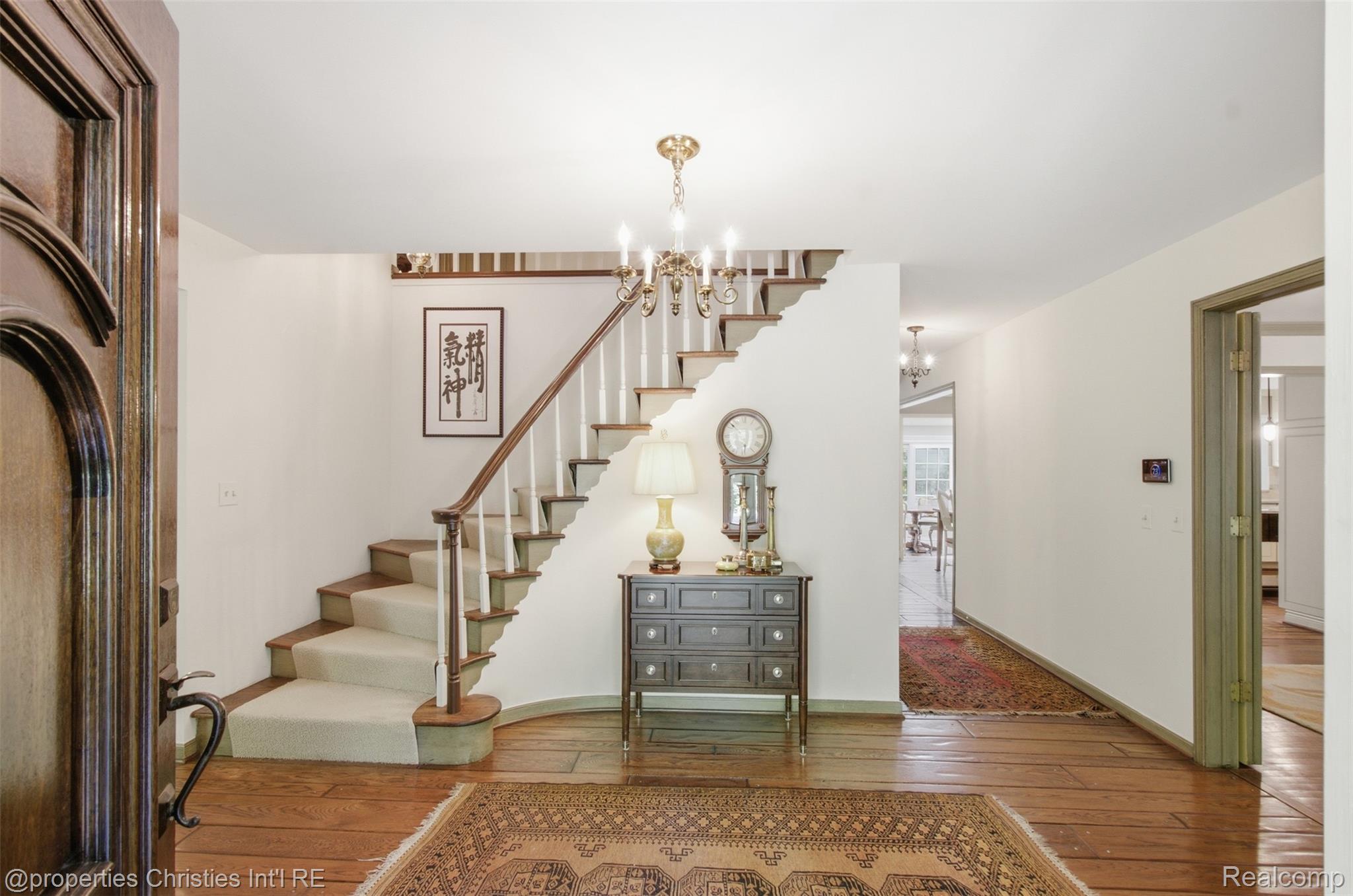 25235 Canterbury Road Franklin, MI 48025 - Photo 6 of 56 Entry foyer featuring hardwood flooring, a winding staircase with carpeted treads and white risers, and a brass chandelier