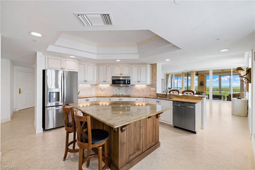 435 Dockside Drive, Unit A804 Naples, FL 34110 - Photo 17 of 50 Kitchen with a breakfast bar area, a peninsula, light stone counters, stainless steel appliances, and decorative backsplash