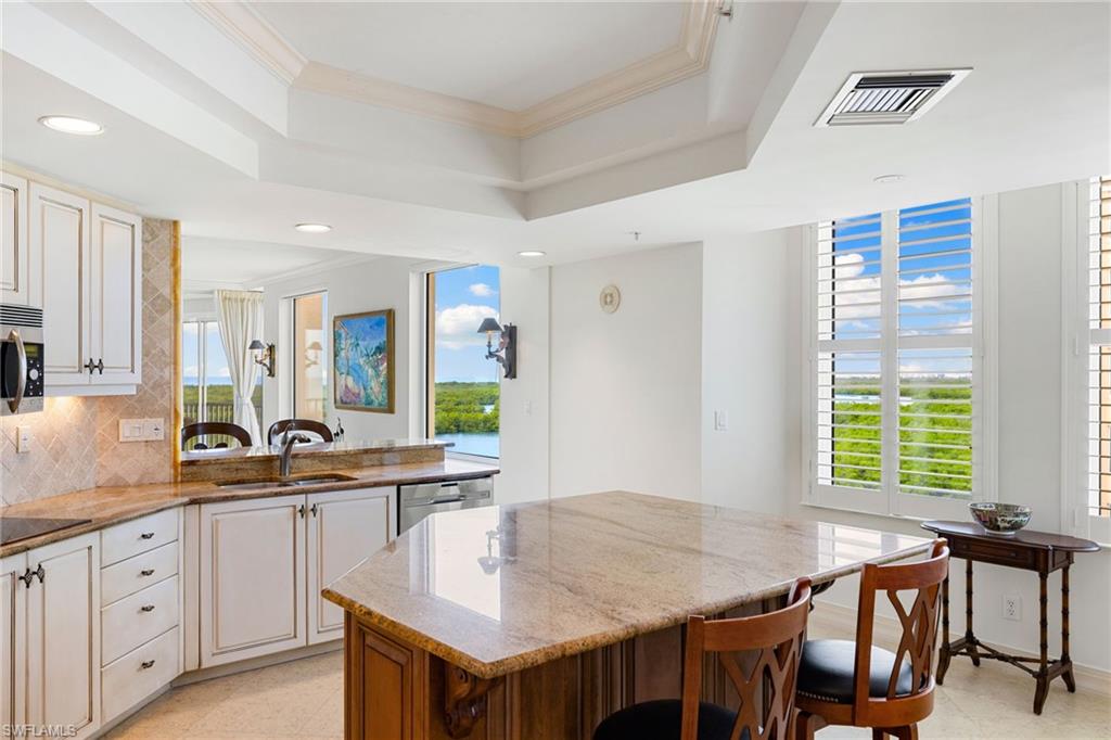 435 Dockside Drive, Unit A804 Naples, FL 34110 - Photo 18 of 50 Kitchen featuring light stone countertops, a kitchen breakfast bar, decorative backsplash, ornamental molding, and a tray ceiling