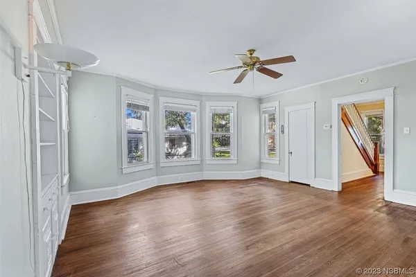 an empty room with wooden floor ceiling fan and windows