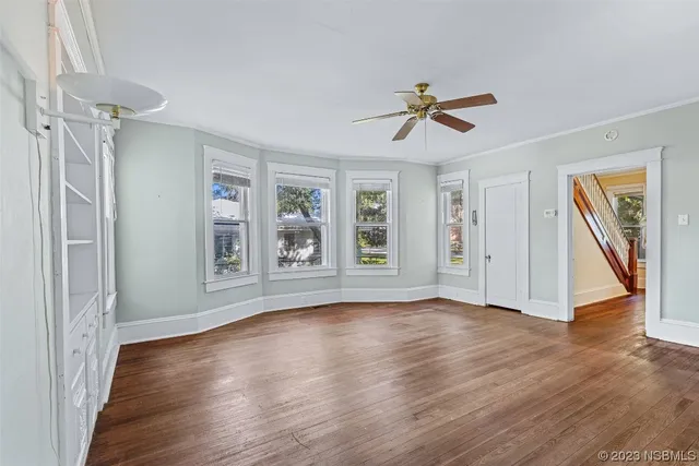 an empty room with wooden floor ceiling fan and windows
