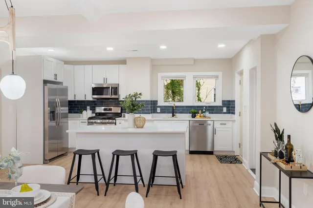 a kitchen with stainless steel appliances kitchen island granite countertop a refrigerator a stove a sink dishwasher and white cabinets with wooden floor