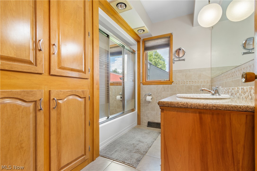 22840 Buck Road Alliance, OH 44601 - Photo 14 of 36 Full bathroom with shower / bath combination with glass door, light tile patterned floors, vanity, tile walls, and a wainscoted wall