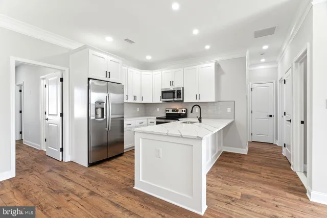 a kitchen with stainless steel appliances a refrigerator stove a sink and white cabinets with wooden floor