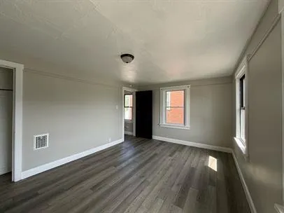 a view of an empty room with wooden floor and a window