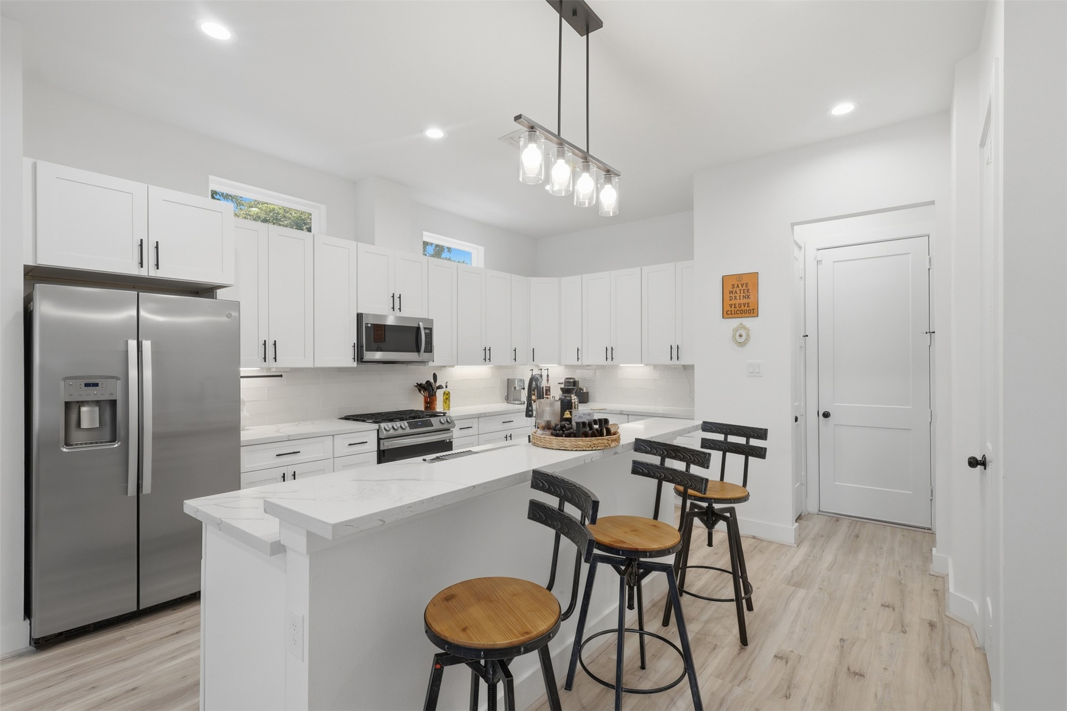 6833 Paris Street Houston, TX 77021 - Photo 9 of 23 This modern kitchen features sleek white cabinetry, stainless steel appliances, and a spacious island with bar seating. Bright and airy, it has recessed lighting and a stylish overhead fixture, complemented by light wood flooring.