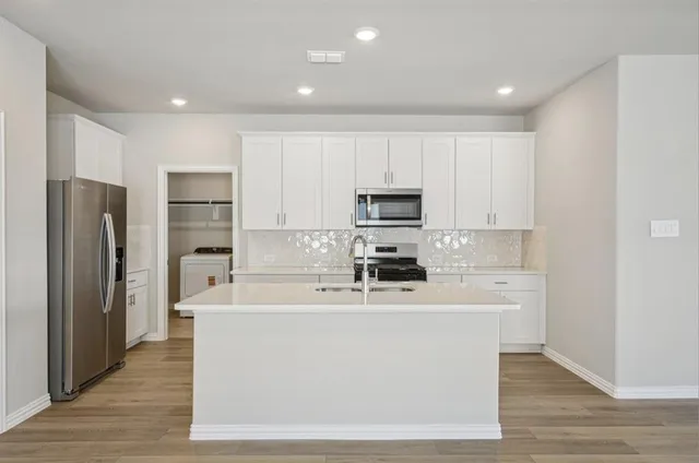 a white kitchen with stainless steel appliances granite countertop a refrigerator a stove a sink and white cabinets with wooden floor