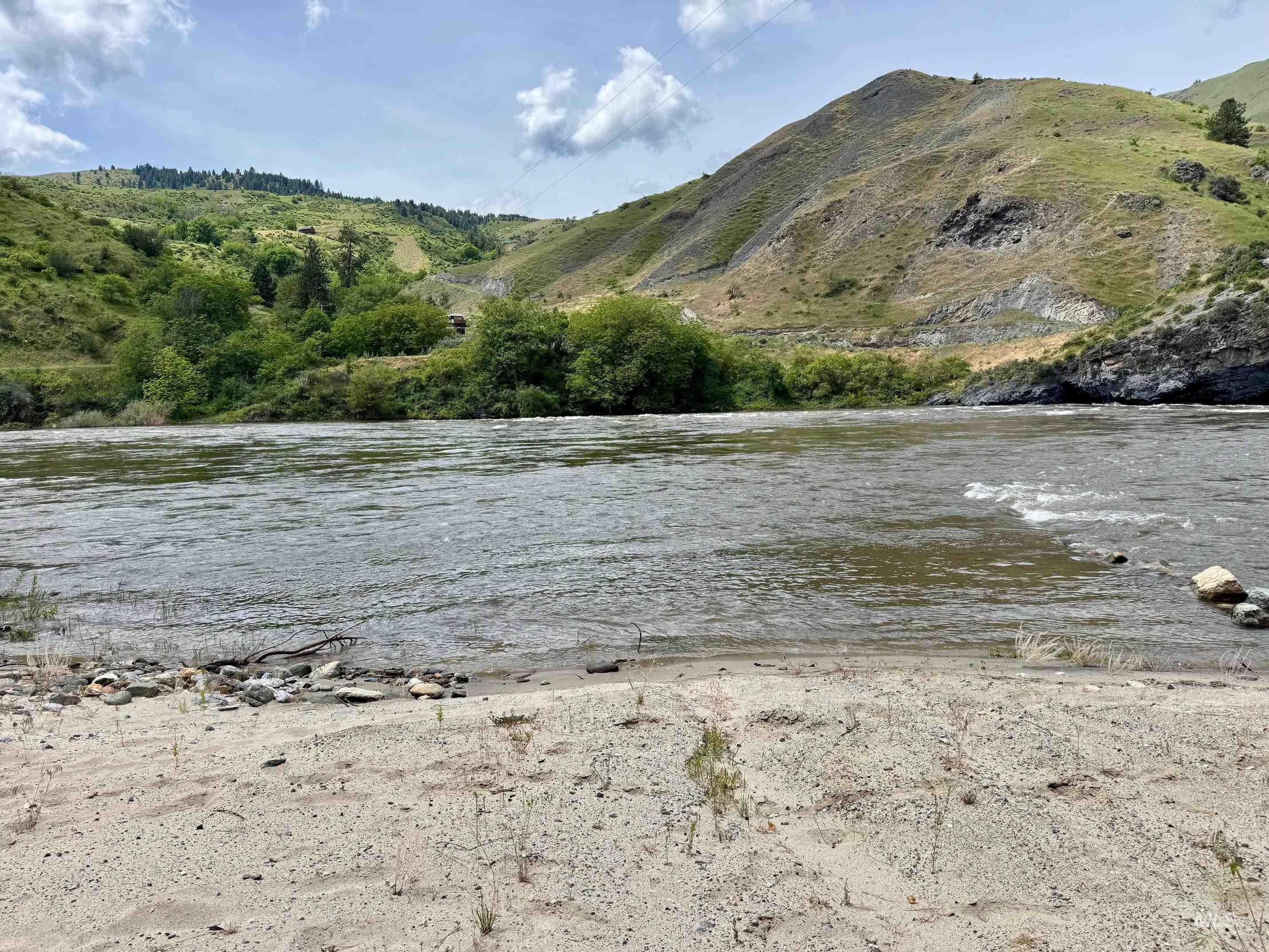 151 Cow Creek Road Lucile, ID 83542 - Photo 49 of 50 River frontage featuring sandy bank, surrounding hillsides with natural vegetation, and a clear sky with scattered clouds