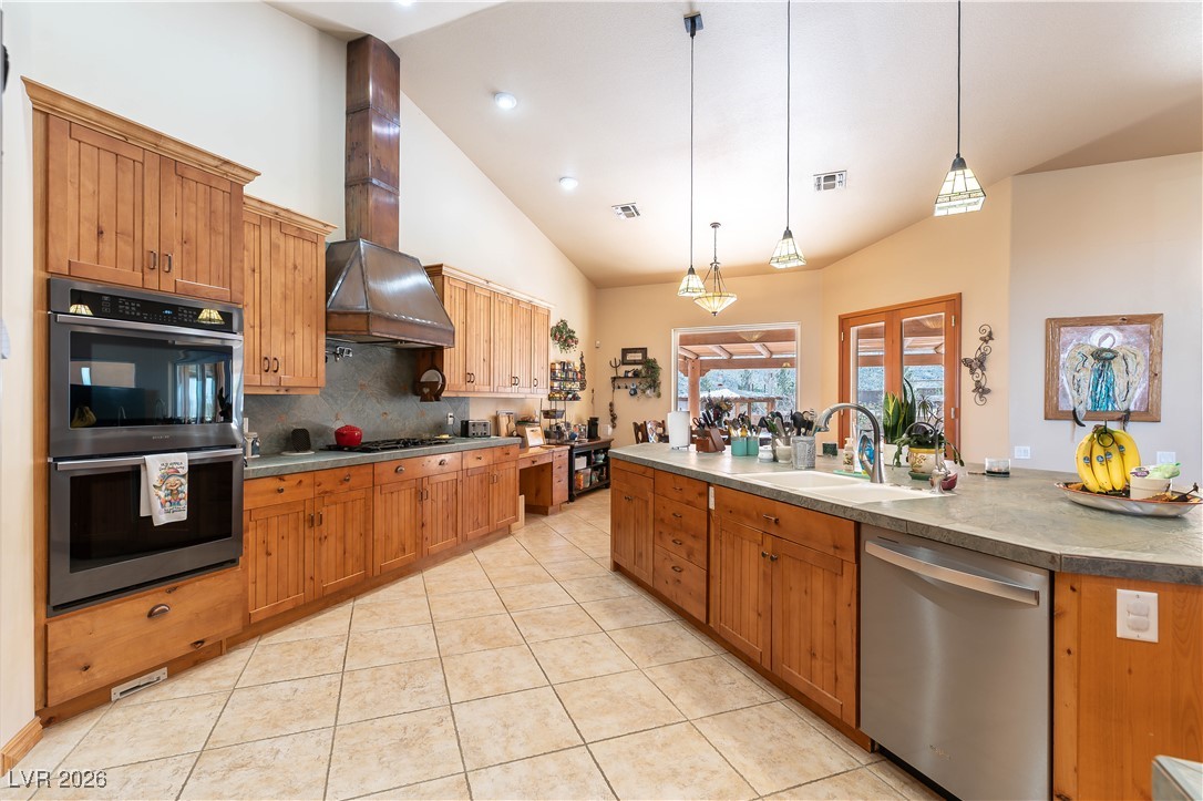 13675 Racel Street Las Vegas, NV 89166 - Photo 12 of 55 Kitchen featuring appliances with stainless steel finishes, brown cabinets, hanging light fixtures, high vaulted ceiling, and light tile patterned flooring