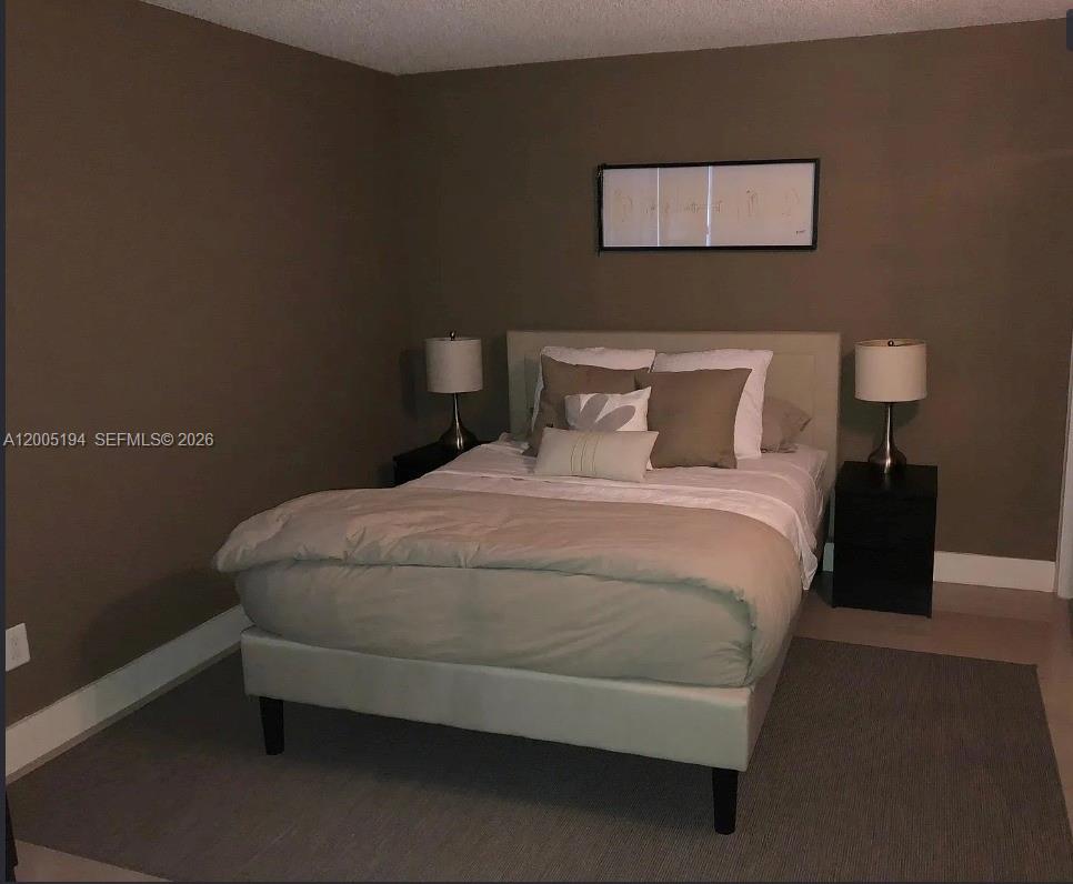 7705 Southwest 86th Street, Unit B211 Miami, FL 33143 - Photo 11 of 22 a bed sitting in a bedroom next to a lamp