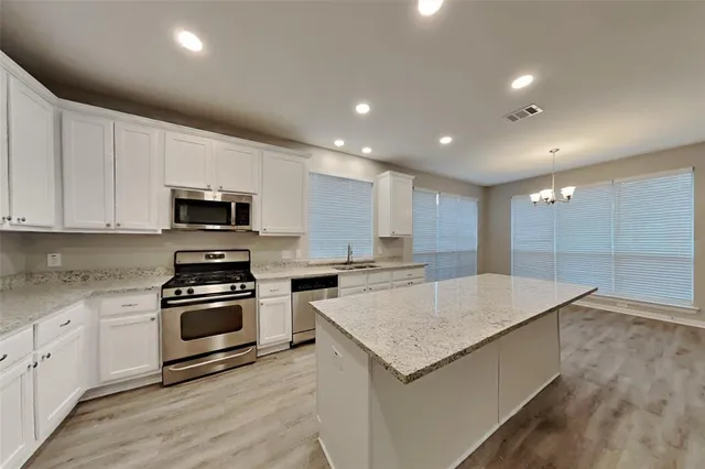 a kitchen with stainless steel appliances a stove top oven a sink a refrigerator white cabinets and wooden floor