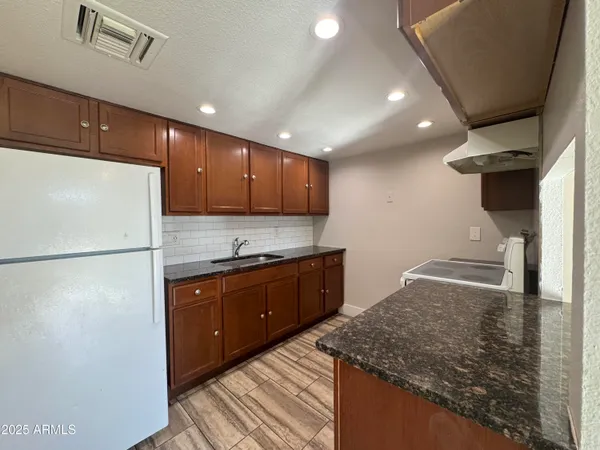 a kitchen with granite countertop a refrigerator a sink and wooden cabinets
