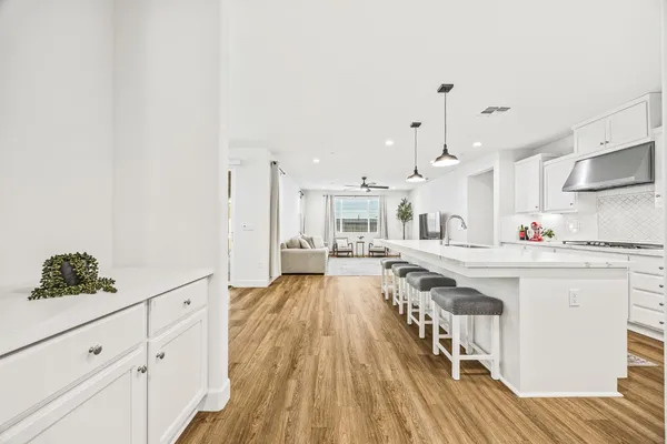 a large white kitchen with kitchen island a stove a sink dishwasher and white cabinets with wooden floor