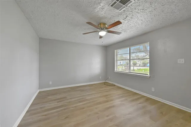 an empty room with wooden floor ceiling fan and windows