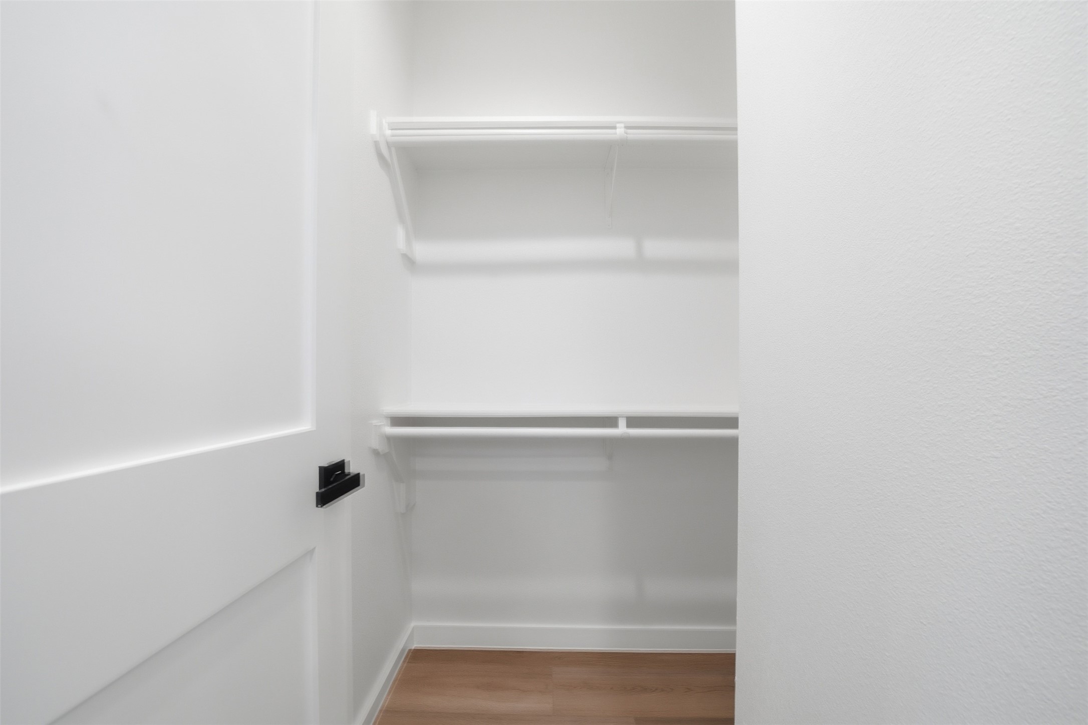 2212 Yellow Jacket Lane, Unit 2 Austin, TX 78741 - Photo 21 of 25 Spacious closet featuring white shelving and hanging rods, white trim, wood-finish flooring, and a white paneled door with matte black hardware