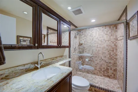 a bathroom with a granite countertop sink a toilet a mirror and shower