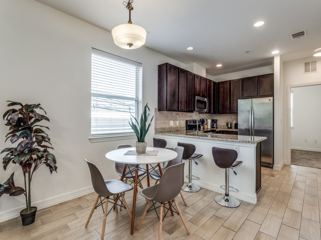 a kitchen with stainless steel appliances kitchen island granite countertop a refrigerator a stove a kitchen island a dining table and chairs with wooden floor
