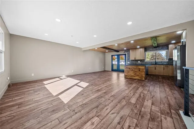 a living room with stainless steel appliances wooden floors and kitchen view