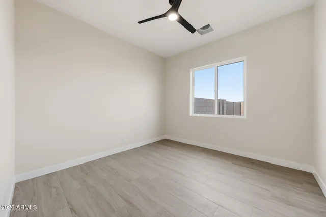 an empty room with wooden floor ceiling fan and windows