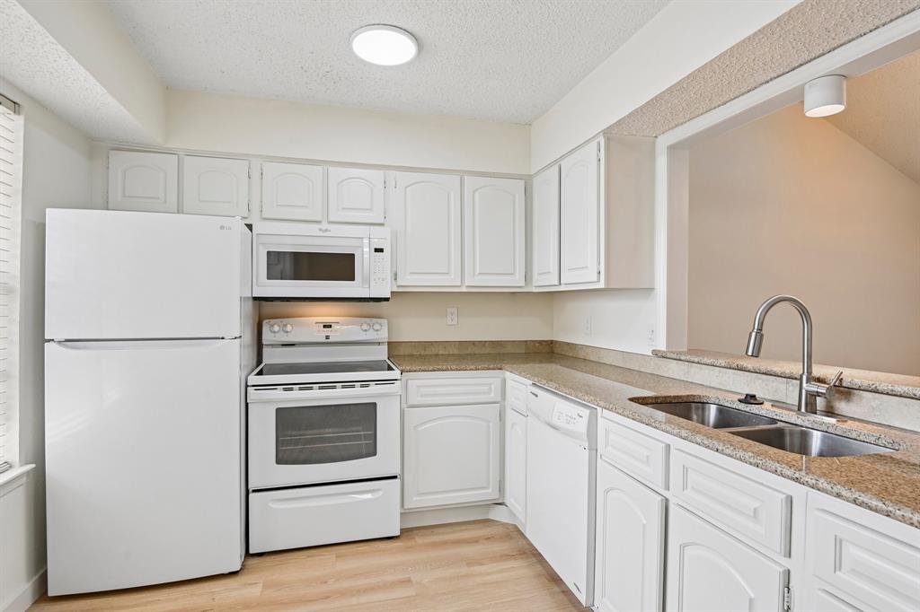 5300 Keller Springs Road, Unit 2055 Dallas, TX 75248 - Photo 4 of 24 Kitchen featuring wood-finish flooring, white cabinetry, granite countertops, and a double basin stainless steel sink with a pull-down faucet