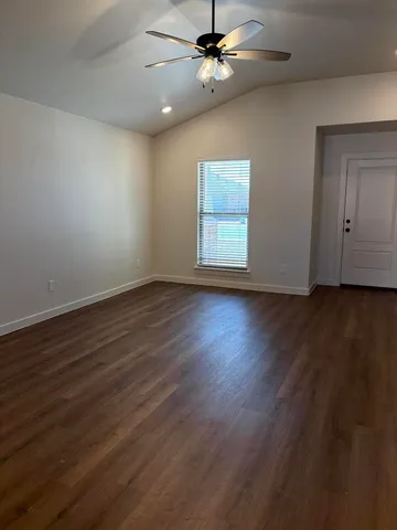 an empty room with wooden floor chandelier fan and windows
