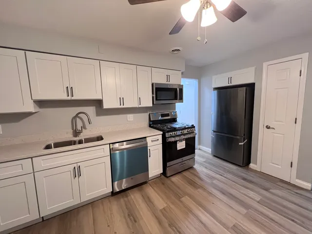 a kitchen with granite countertop a refrigerator a sink dishwasher a stove and white cabinets with wooden floor