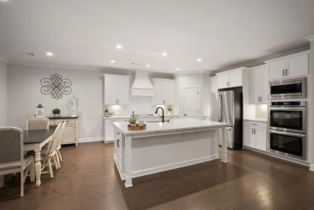 a kitchen with stainless steel appliances kitchen island granite countertop a stove a sink a refrigerator and white cabinets with wooden floor