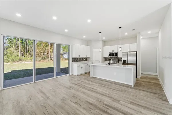 a large kitchen with kitchen island a stove a refrigerator and white cabinets with wooden floor