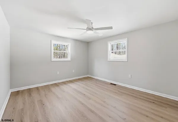 an empty room with wooden floor ceiling fan and windows