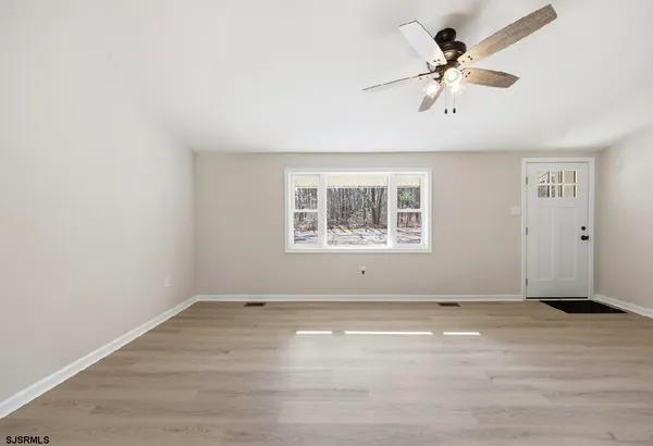an empty room with wooden floor chandelier fan and windows