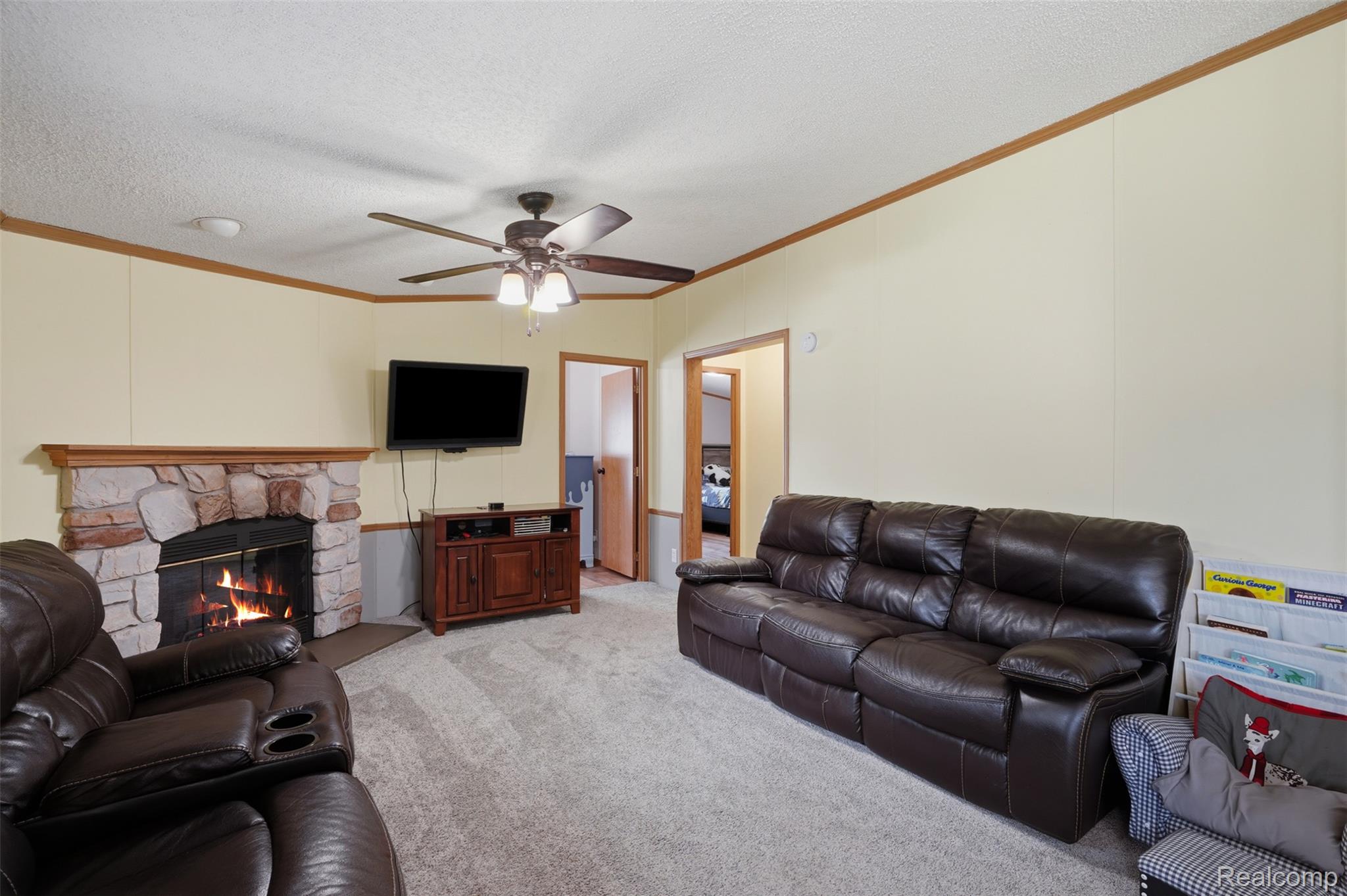 4634 Butternut Street Clarkston, MI 48348 - Photo 13 of 28 Living area featuring a stone-clad fireplace with a wood mantel, a ceiling fan with integrated lighting, light-toned walls, and soft carpet flooring