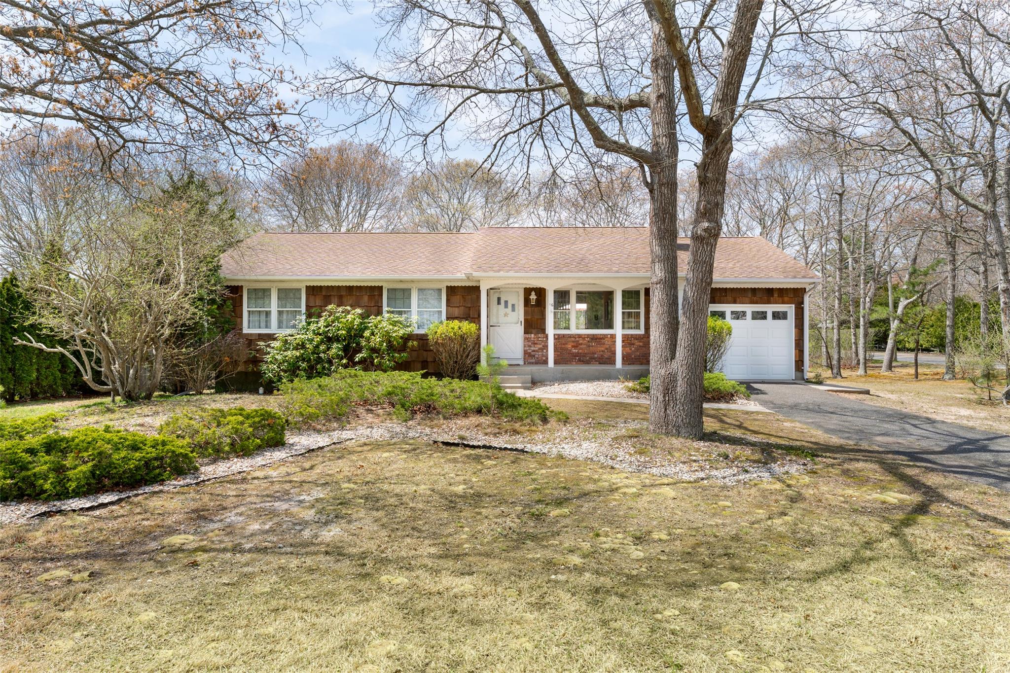 Ranch-style home featuring covered porch, a shingled roof, driveway, and an attached garage