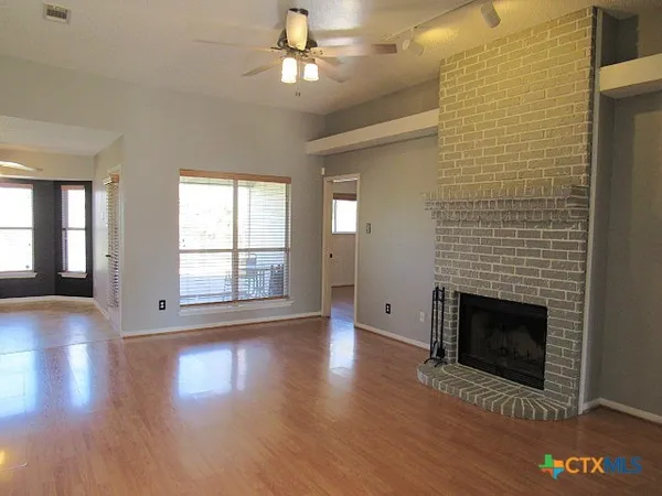 a view of an empty room with wooden floor fireplace and a window