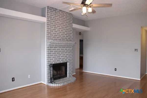 a view of an empty room with wooden floor and a fireplace