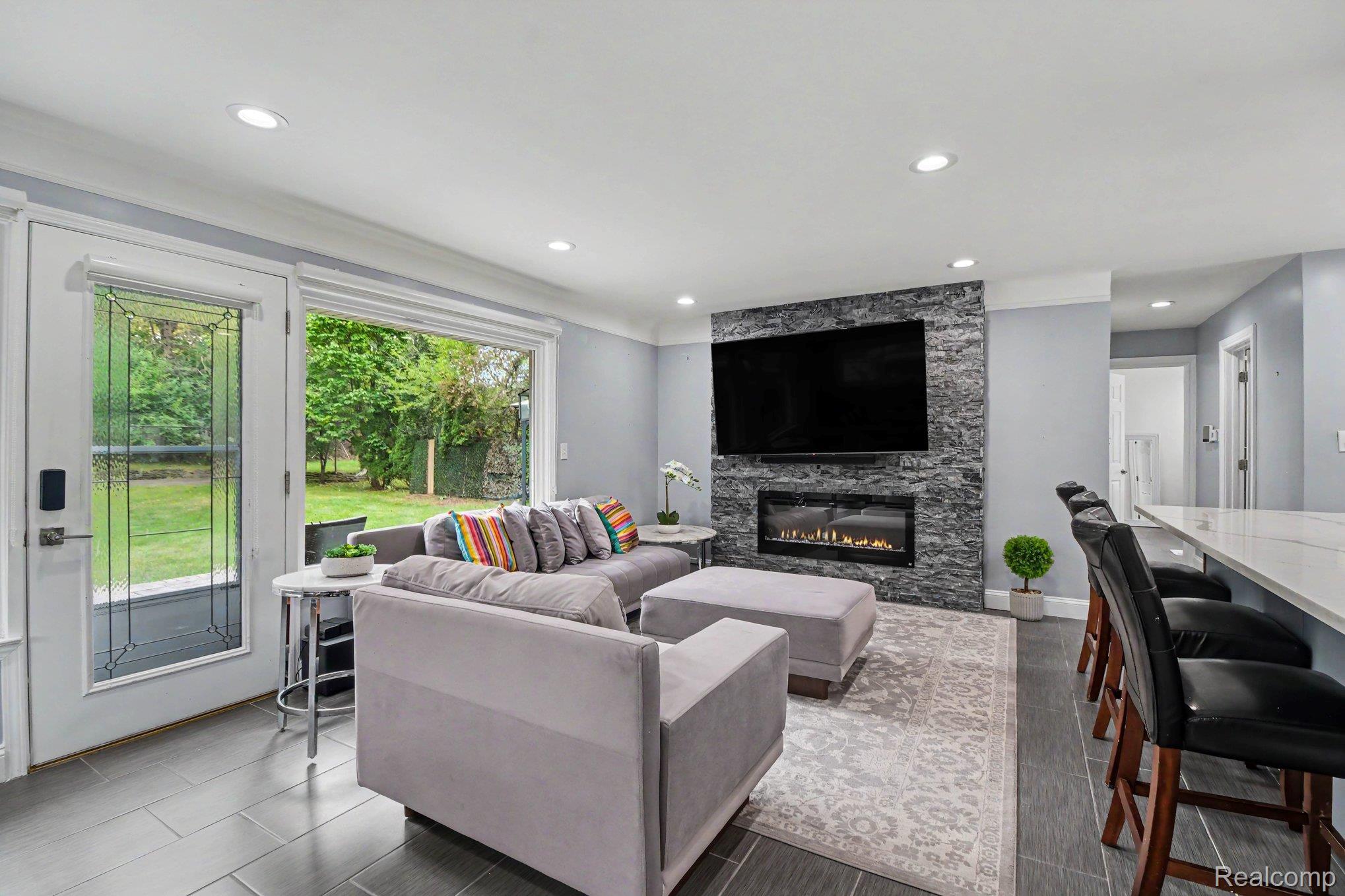 2373 Rutherford Road Bloomfield Hills, MI 48302 - Photo 10 of 28 Recessed lighting, tiled flooring, built-in electric fireplace with stacked stone surround, large window with outdoor visibility, and a breakfast bar with a light-toned countertop