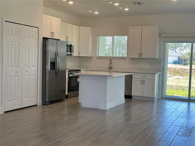 a kitchen with stainless steel appliances granite countertop a refrigerator a sink dishwasher a stove and white countertops with wooden floor