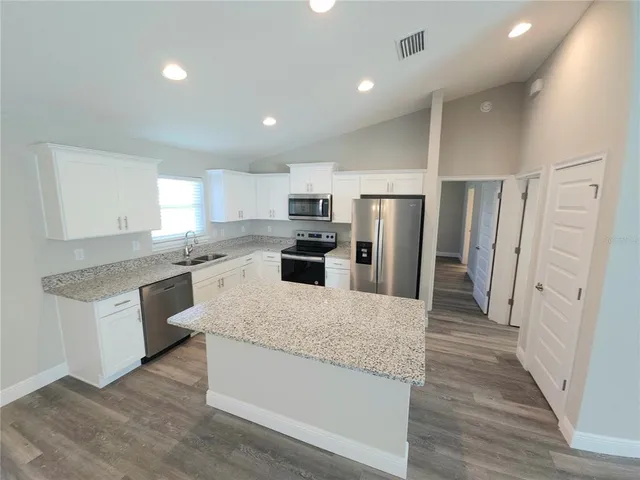 a large kitchen with stainless steel appliances granite countertop a refrigerator a sink a stove and white cabinets with wooden floor