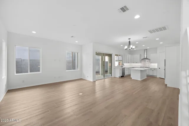a view of an empty room with wooden floor and a kitchen