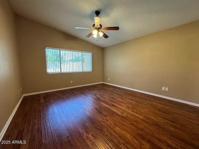 a view of an empty room with wooden floor and a ceiling fan