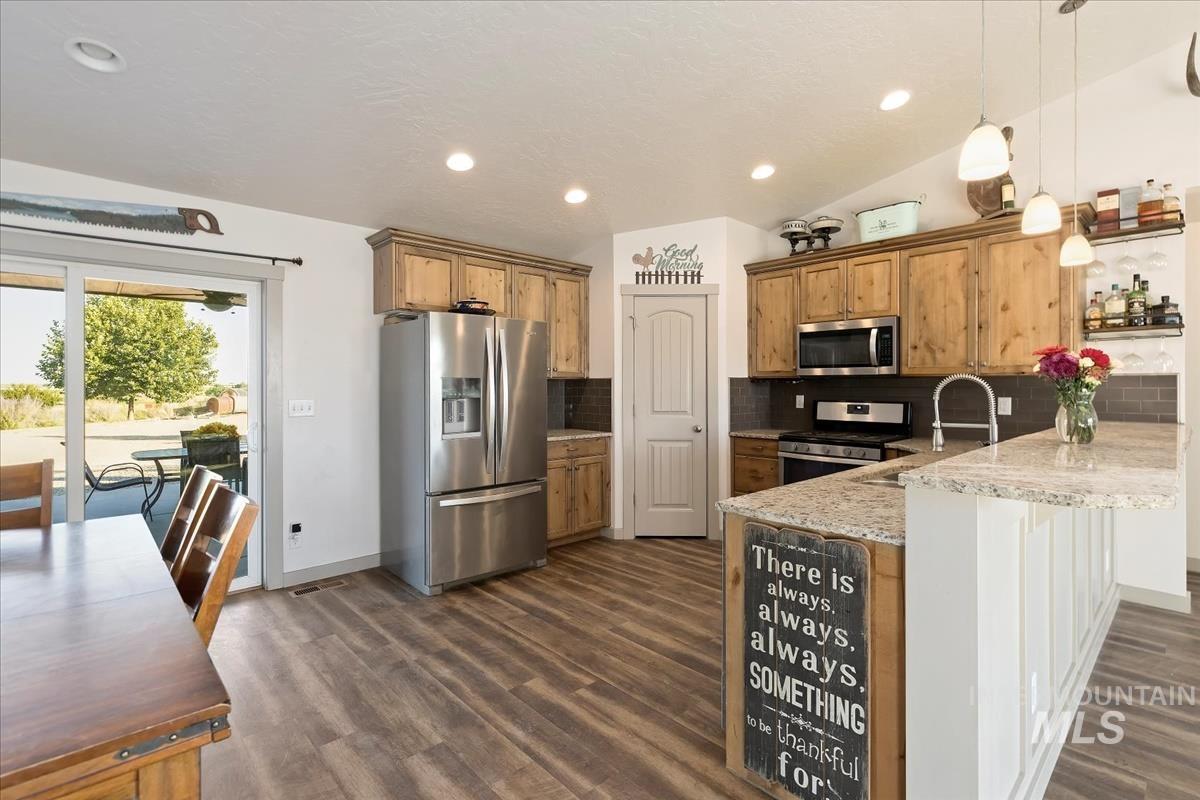17571 Goodson Road Caldwell, ID 83607 - Photo 6 of 36 Kitchen featuring stainless steel appliances, backsplash, decorative light fixtures, light stone counters, and a kitchen breakfast bar