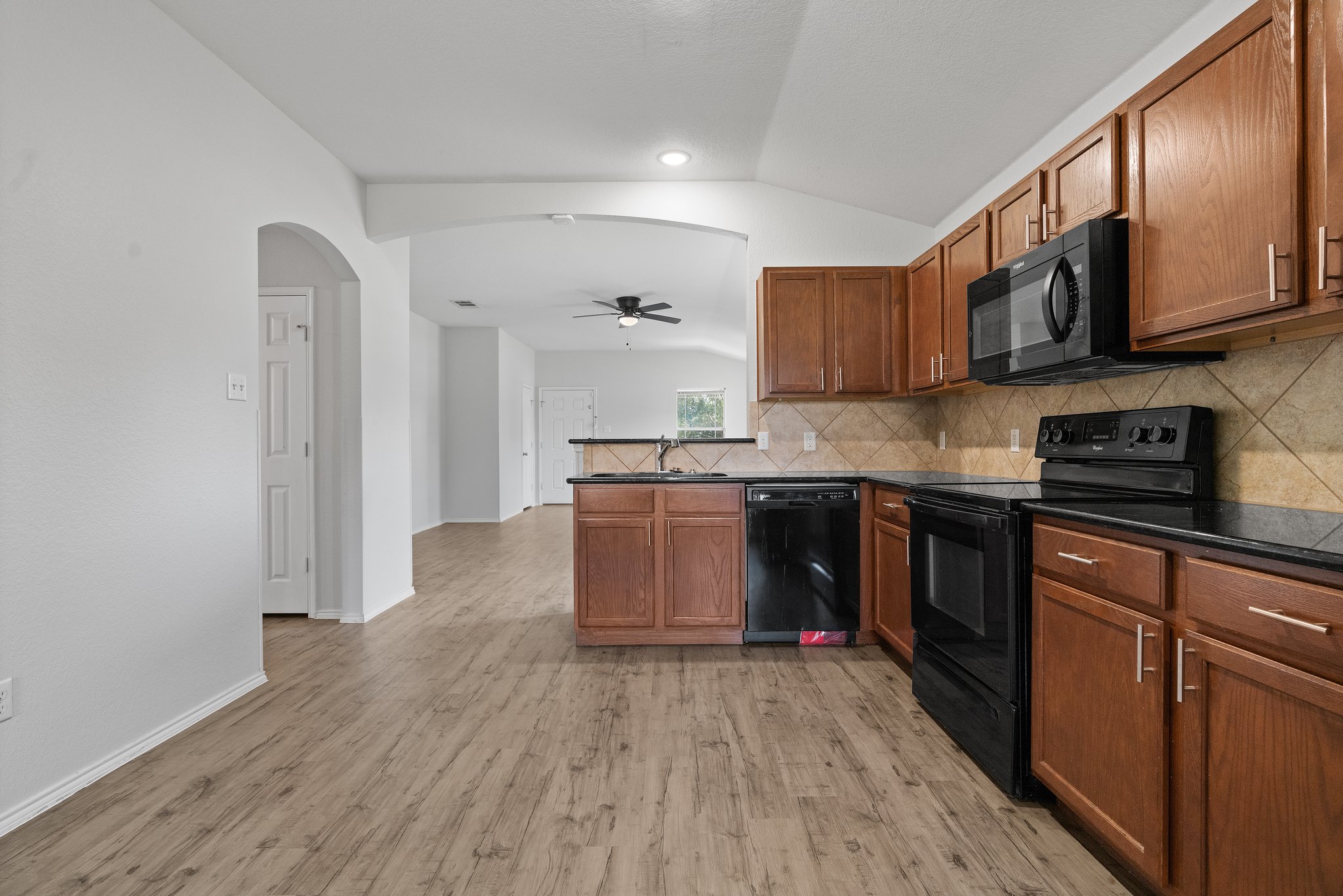 5800 Maciver Drive Austin, TX 78754 - Photo 10 of 27 Kitchen featuring black appliances, lofted ceiling, brown cabinetry, arched walkways, and a ceiling fan