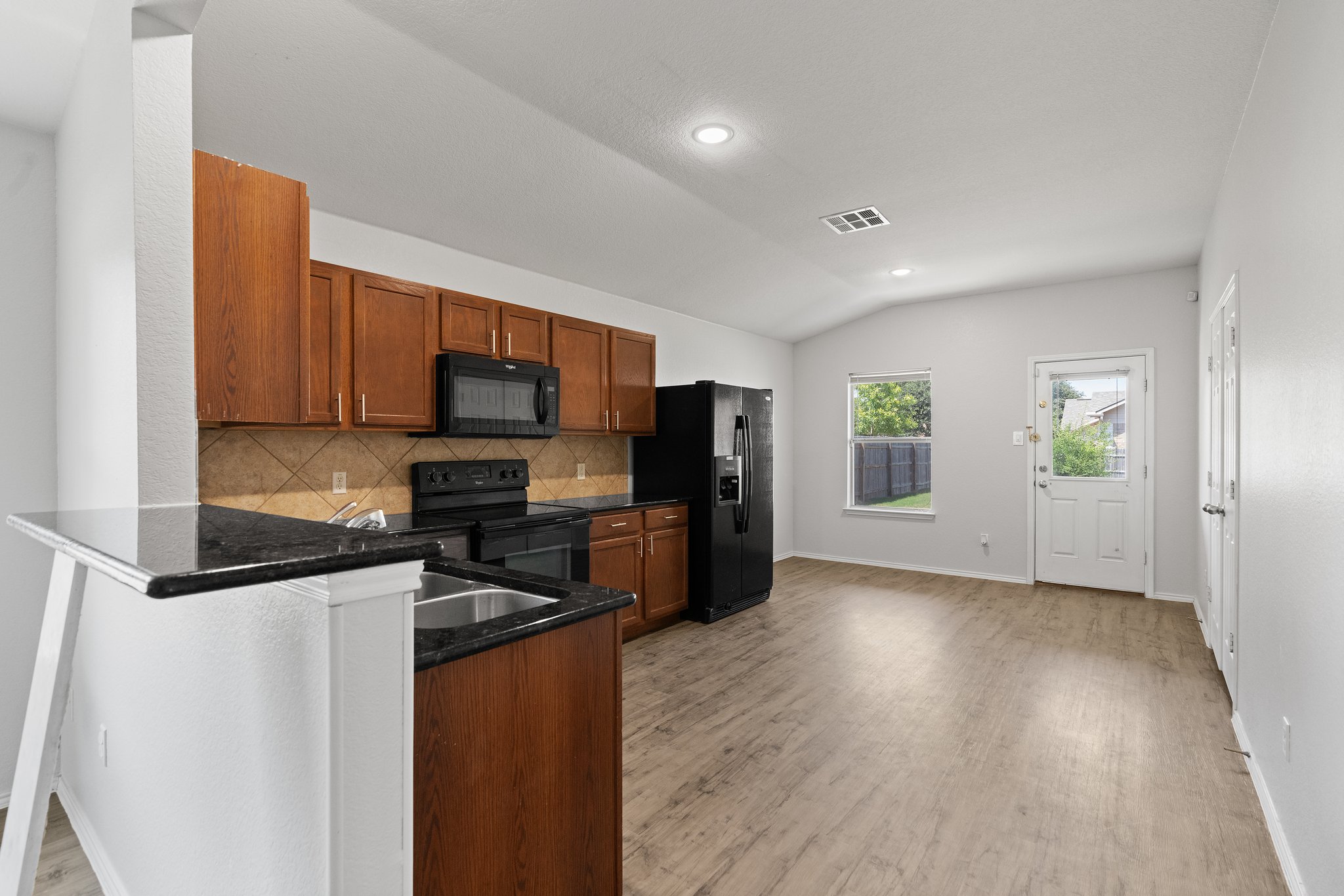 5800 Maciver Drive Austin, TX 78754 - Photo 8 of 27 Kitchen featuring black appliances, brown cabinets, vaulted ceiling, backsplash, and dark stone countertops