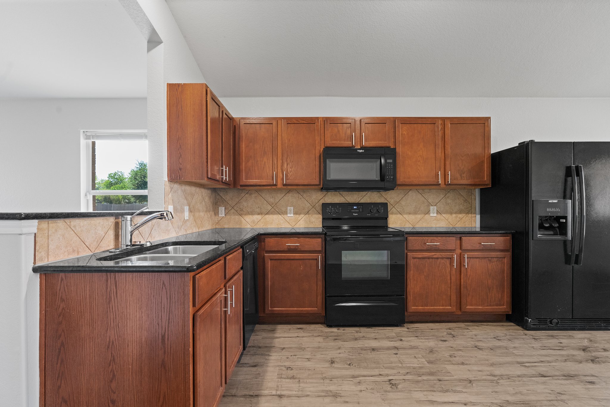 5800 Maciver Drive Austin, TX 78754 - Photo 9 of 27 Kitchen featuring black appliances, brown cabinetry, dark stone counters, and light wood-style flooring