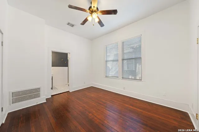 an empty room with wooden floor chandelier fan and windows