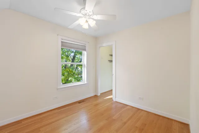 an empty room with wooden floor ceiling fan and windows