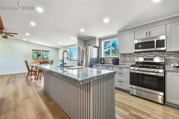 a kitchen with stainless steel appliances granite countertop a stove top oven a sink dishwasher a dining table and chairs with wooden floor