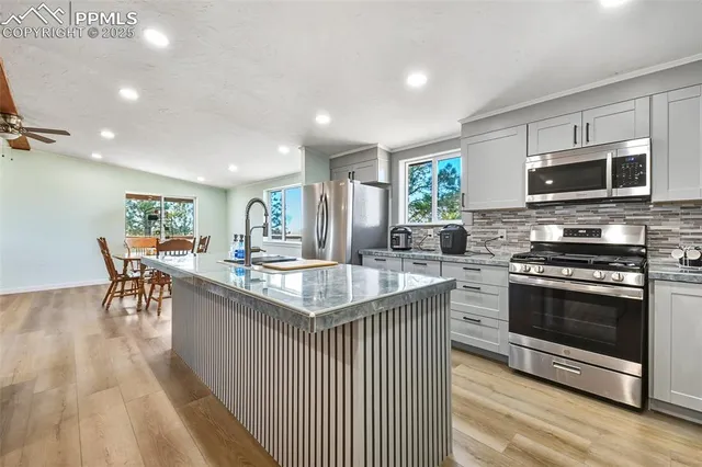 a kitchen with stainless steel appliances granite countertop a stove top oven a sink dishwasher a dining table and chairs with wooden floor