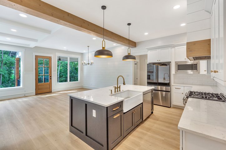 A contemporary kitchen and living area unfolds, showcasing light wood flooring and a kitchen island with a farmhouse sink.