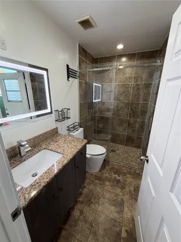 a bathroom with a granite countertop sink a toilet a mirror and shower